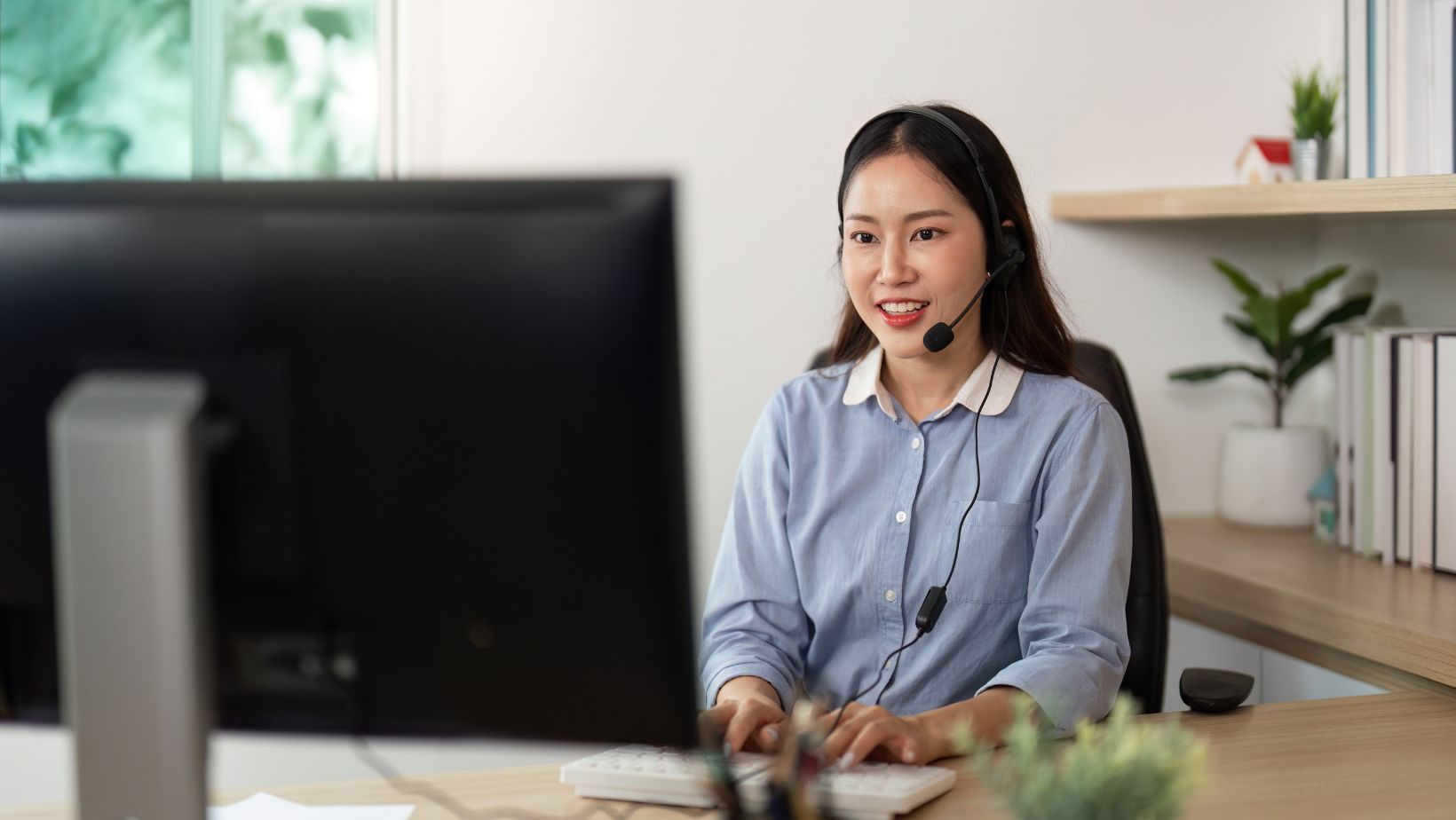 Woman on her headset working from home and communicating with someone on their computer screen
