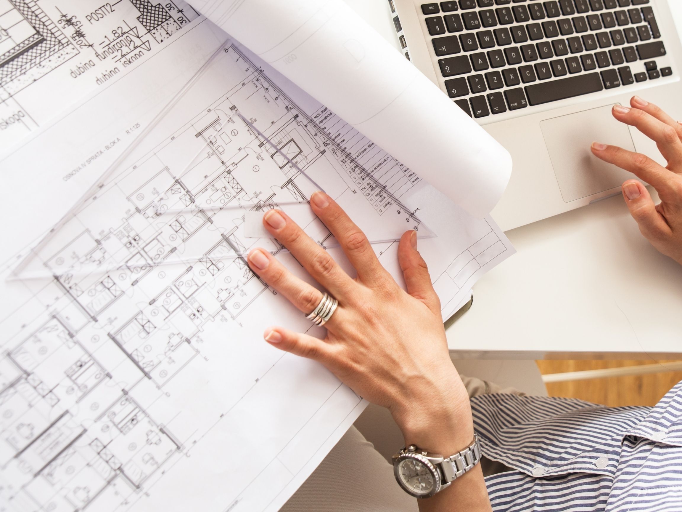 Overhead shot of architect's hand on blueprints while cross referencing with SeekBeak virtual tour on laptop
